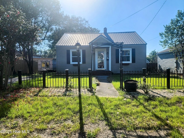 bungalow-style home featuring a fenced front yard, a chimney, metal roof, and a front lawn