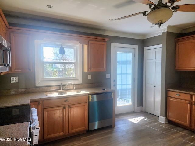 kitchen featuring wood finished floors, brown cabinetry, a sink, appliances with stainless steel finishes, and crown molding