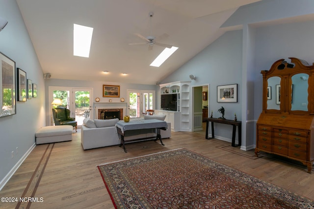 living room with high vaulted ceiling, ceiling fan, light wood-type flooring, and a skylight