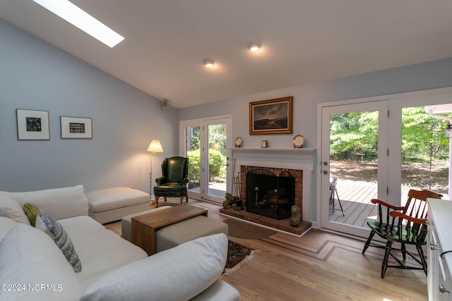 living room with high vaulted ceiling, light hardwood / wood-style floors, a fireplace, and a skylight