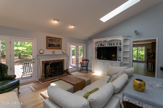 living room with high vaulted ceiling, a brick fireplace, a skylight, and light hardwood / wood-style flooring