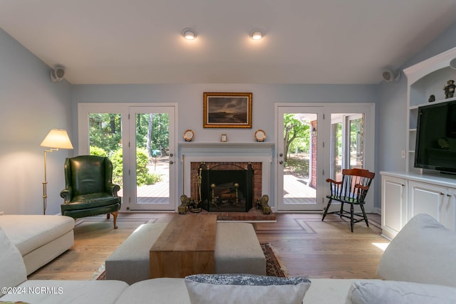 living room featuring plenty of natural light, light wood-type flooring, and a brick fireplace