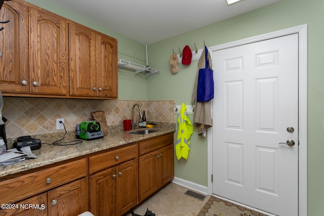 kitchen with sink, light stone counters, backsplash, and light tile floors