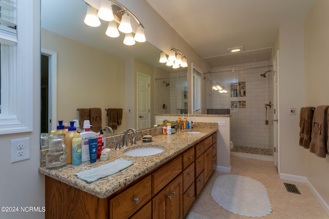 bathroom with tiled shower, tile flooring, and dual vanity