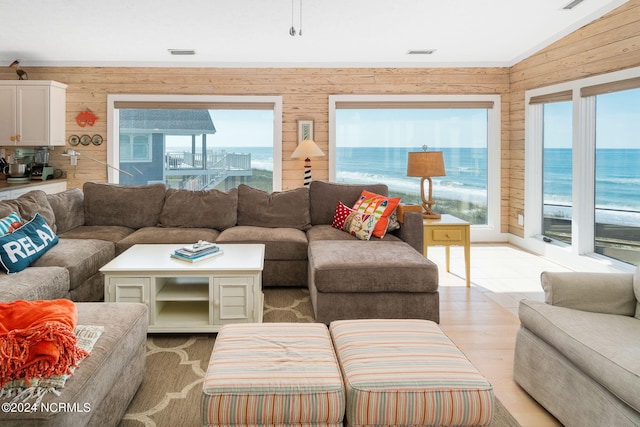 living room featuring plenty of natural light, wood walls, a water view, and vaulted ceiling