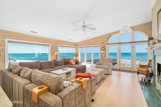 living room with a fireplace, a water view, ceiling fan, and a healthy amount of sunlight