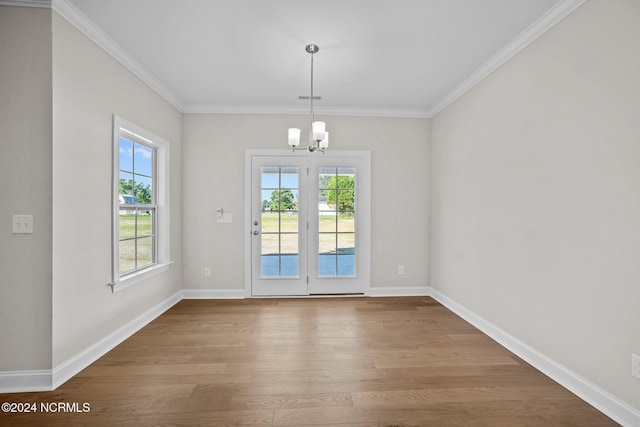unfurnished dining area featuring wood finished floors, a chandelier, plenty of natural light, baseboards, and ornamental molding