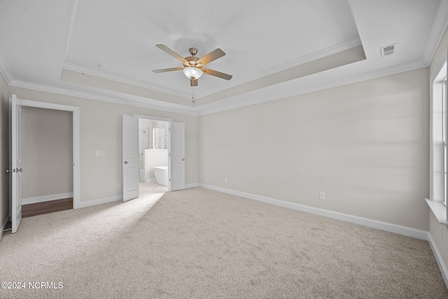 unfurnished bedroom featuring a tray ceiling, light carpet, crown molding, baseboards, and ensuite bathroom