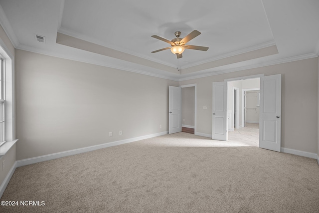 unfurnished bedroom with a tray ceiling, ornamental molding, light carpet, baseboards, and a ceiling fan