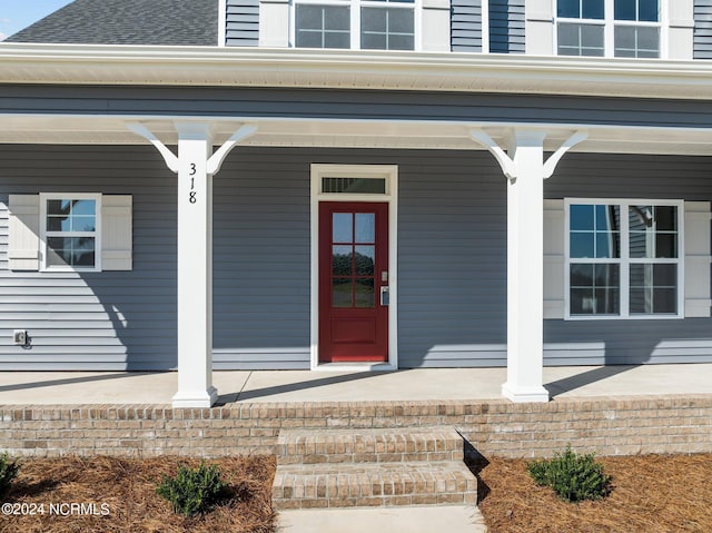 property entrance with covered porch and a shingled roof