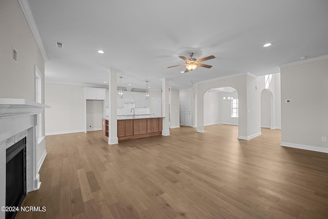 unfurnished living room featuring arched walkways, a ceiling fan, a sink, light wood-type flooring, and crown molding