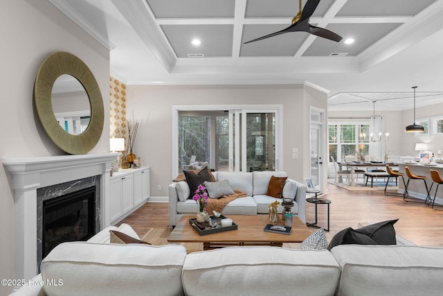 living room featuring coffered ceiling, ceiling fan with notable chandelier, a fireplace, and light hardwood / wood-style flooring