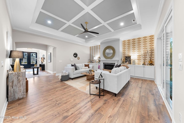 living room featuring ornamental molding, coffered ceiling, a high end fireplace, light hardwood / wood-style floors, and french doors