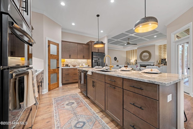 kitchen featuring coffered ceiling, a center island with sink, pendant lighting, light stone countertops, and black appliances