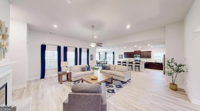 living room featuring a high end fireplace, ceiling fan, and light hardwood / wood-style floors