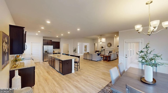 kitchen with light hardwood / wood-style floors, stainless steel appliances, a kitchen breakfast bar, an island with sink, and pendant lighting