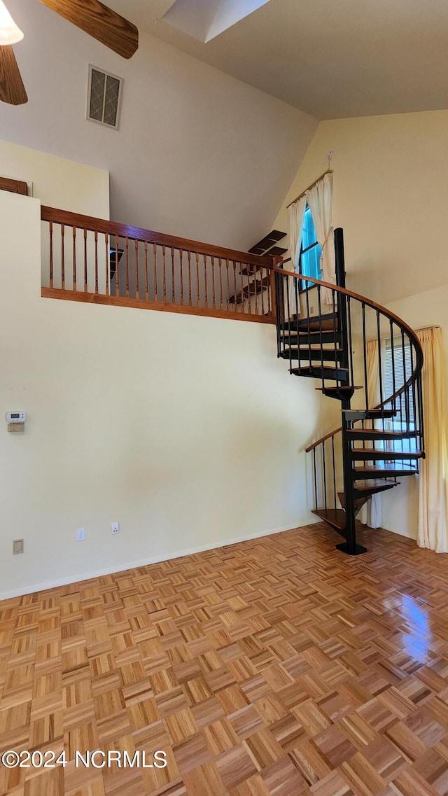 stairs with a towering ceiling, ceiling fan, and light parquet flooring