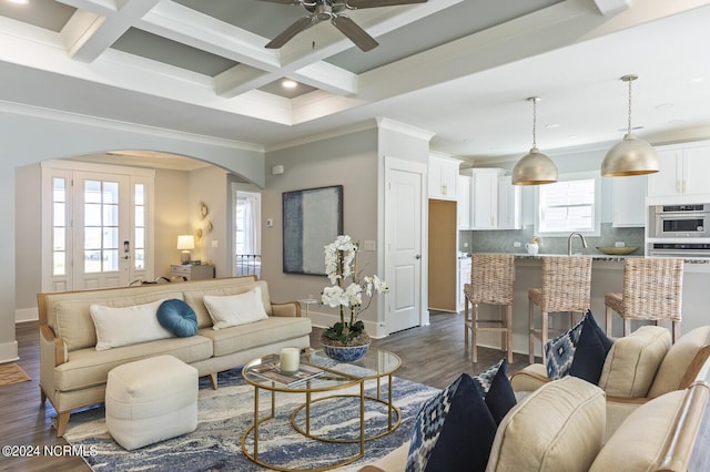 living area featuring arched walkways, dark wood finished floors, crown molding, and coffered ceiling