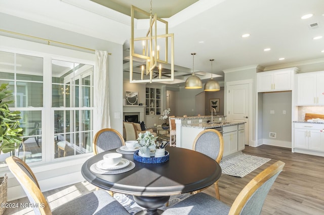 dining room with an inviting chandelier, sink, crown molding, and light wood-type flooring