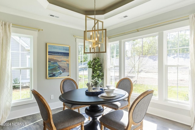 dining area with a tray ceiling, plenty of natural light, visible vents, a notable chandelier, and wood finished floors