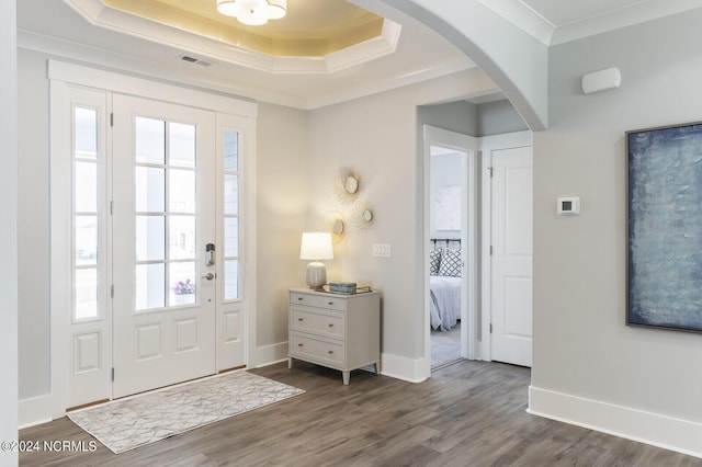foyer entrance with arched walkways, a tray ceiling, dark wood finished floors, ornamental molding, and visible vents