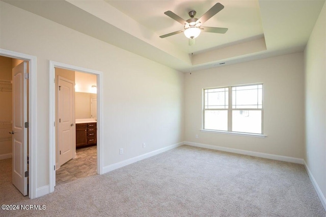 unfurnished bedroom featuring light carpet, connected bathroom, a raised ceiling, and a walk in closet