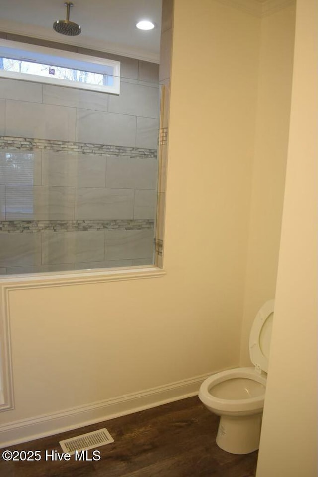 bathroom featuring toilet, wood-type flooring, and a tile shower