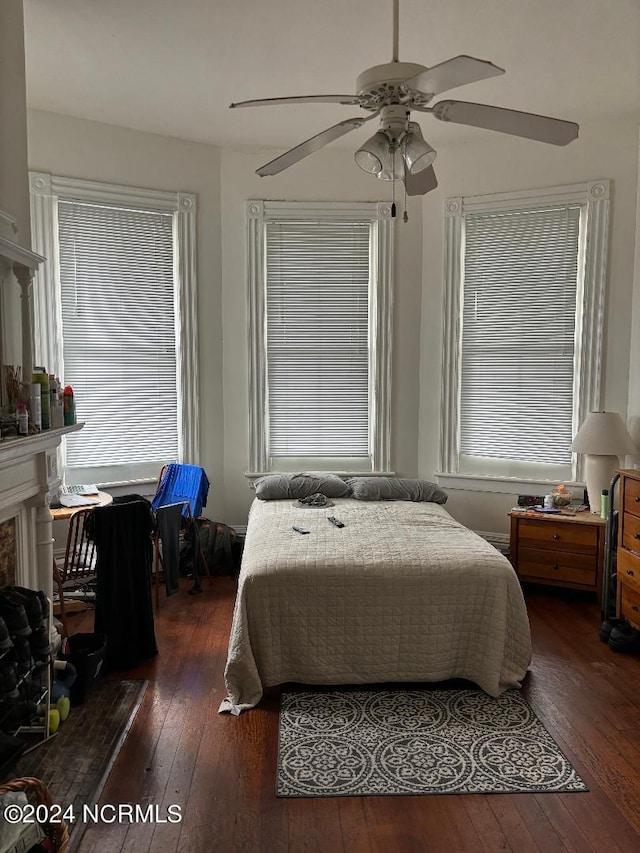 bedroom with multiple windows, dark hardwood / wood-style floors, ceiling fan, and a premium fireplace