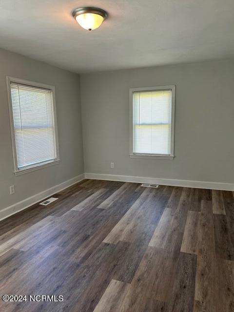 empty room with plenty of natural light, visible vents, dark wood finished floors, and baseboards