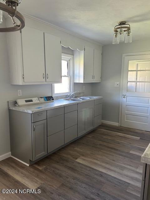 kitchen with dark wood-type flooring, light countertops, a sink, and baseboards