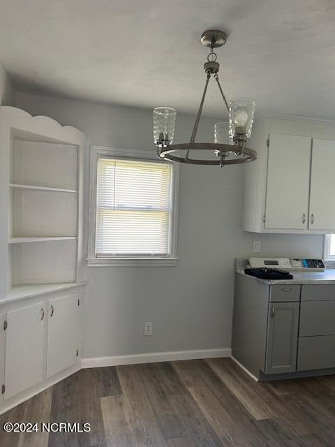 unfurnished dining area with an inviting chandelier, baseboards, and dark wood finished floors