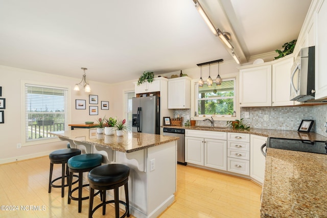 kitchen featuring stainless steel appliances, white cabinetry, hanging light fixtures, and a center island