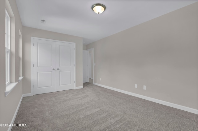 unfurnished bedroom with multiple windows, light colored carpet, and a closet