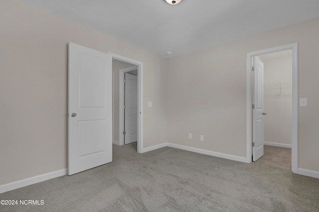 unfurnished bedroom featuring a walk in closet, a closet, and light colored carpet