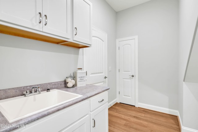washroom with baseboards, light wood-type flooring, and a sink
