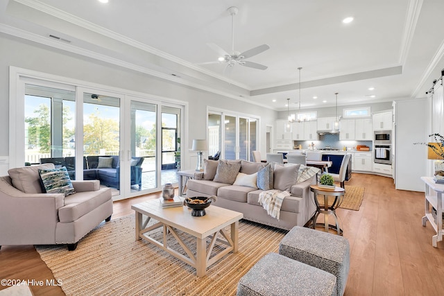 living room with a tray ceiling, plenty of natural light, light hardwood / wood-style floors, and ceiling fan with notable chandelier