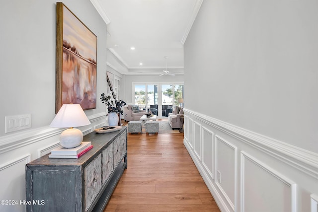 hall featuring recessed lighting, light wood-style flooring, crown molding, a wainscoted wall, and a decorative wall