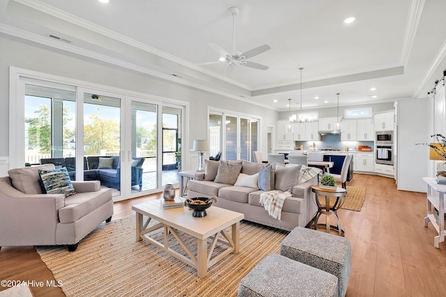 living room with ornamental molding, light wood-type flooring, a tray ceiling, recessed lighting, and ceiling fan with notable chandelier