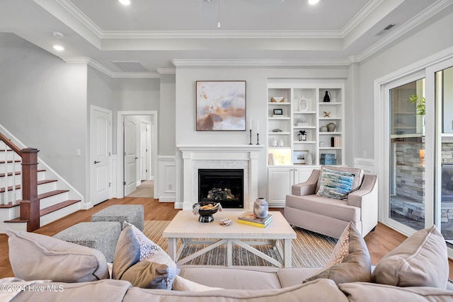 living area featuring light wood-type flooring, a fireplace, stairs, visible vents, and a tray ceiling