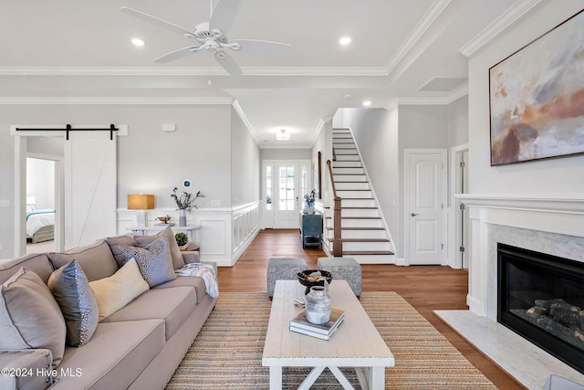 living area with ornamental molding, a ceiling fan, a barn door, a high end fireplace, and wood finished floors