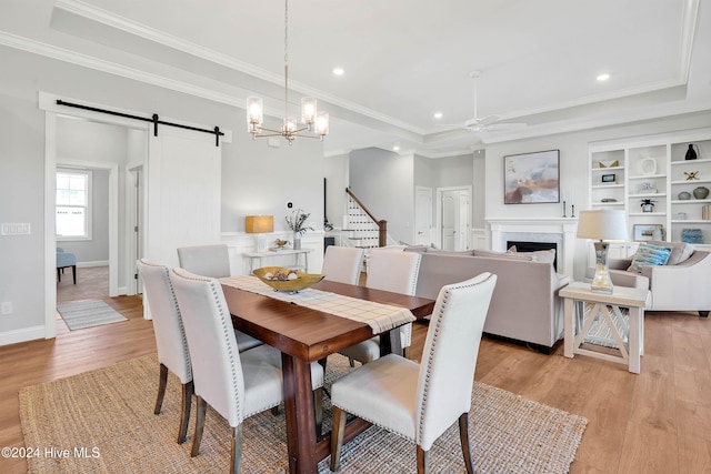 dining space featuring ceiling fan with notable chandelier, a barn door, light hardwood / wood-style floors, and crown molding