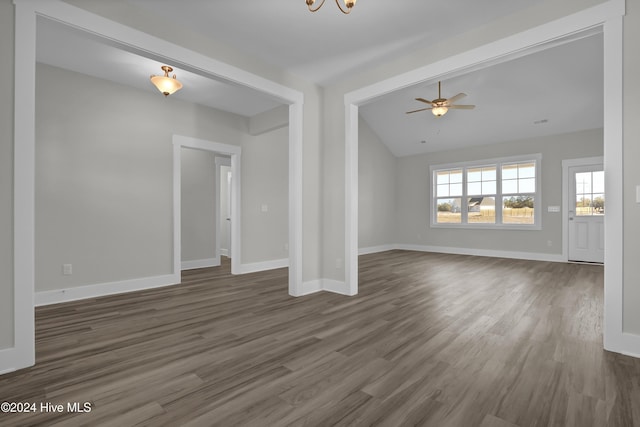 unfurnished living room with ceiling fan with notable chandelier, dark hardwood / wood-style floors, and vaulted ceiling