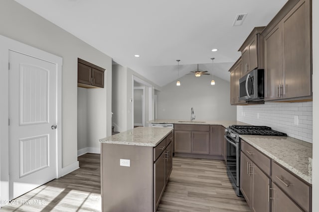 kitchen featuring kitchen peninsula, appliances with stainless steel finishes, light stone countertops, vaulted ceiling, and sink