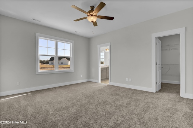 unfurnished bedroom featuring light carpet, ceiling fan, a spacious closet, connected bathroom, and a closet