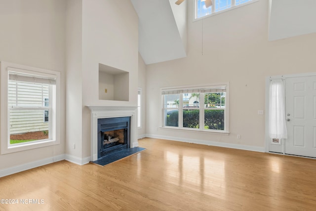 unfurnished living room with ceiling fan, a towering ceiling, and light wood-type flooring