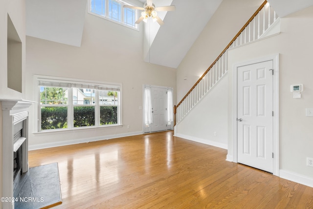 unfurnished living room with ceiling fan, a towering ceiling, and light wood-type flooring