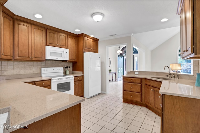 kitchen with lofted ceiling, light stone countertops, white appliances, and sink