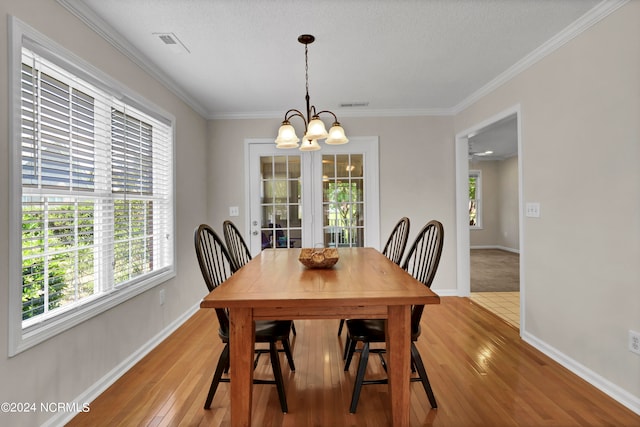 dining area featuring a textured ceiling, crown molding, a notable chandelier, and light wood-type flooring