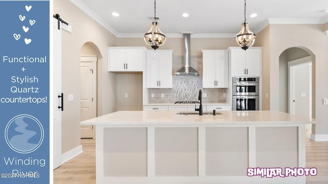 kitchen featuring a center island with sink, wall chimney exhaust hood, a barn door, and stainless steel appliances