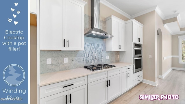 kitchen featuring wall chimney exhaust hood, stainless steel appliances, backsplash, white cabinets, and ornamental molding